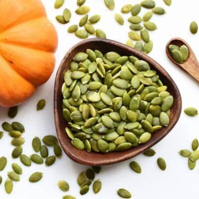 Pumpkin seeds are kept in a wooden bowl with a wooden spoon along with a pumpkin.